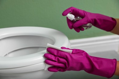 Photo of Woman disinfecting toilet seat in restroom, closeup