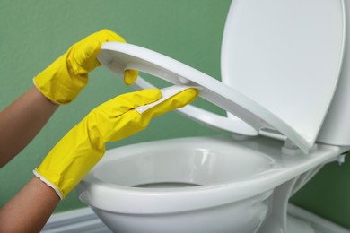 Photo of Woman cleaning toilet seat in restroom, closeup