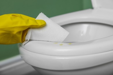 Photo of Woman wiping urine drops from toilet seat in restroom, closeup