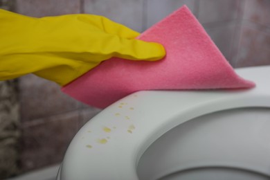 Photo of Woman wiping urine drops from toilet seat in restroom, closeup