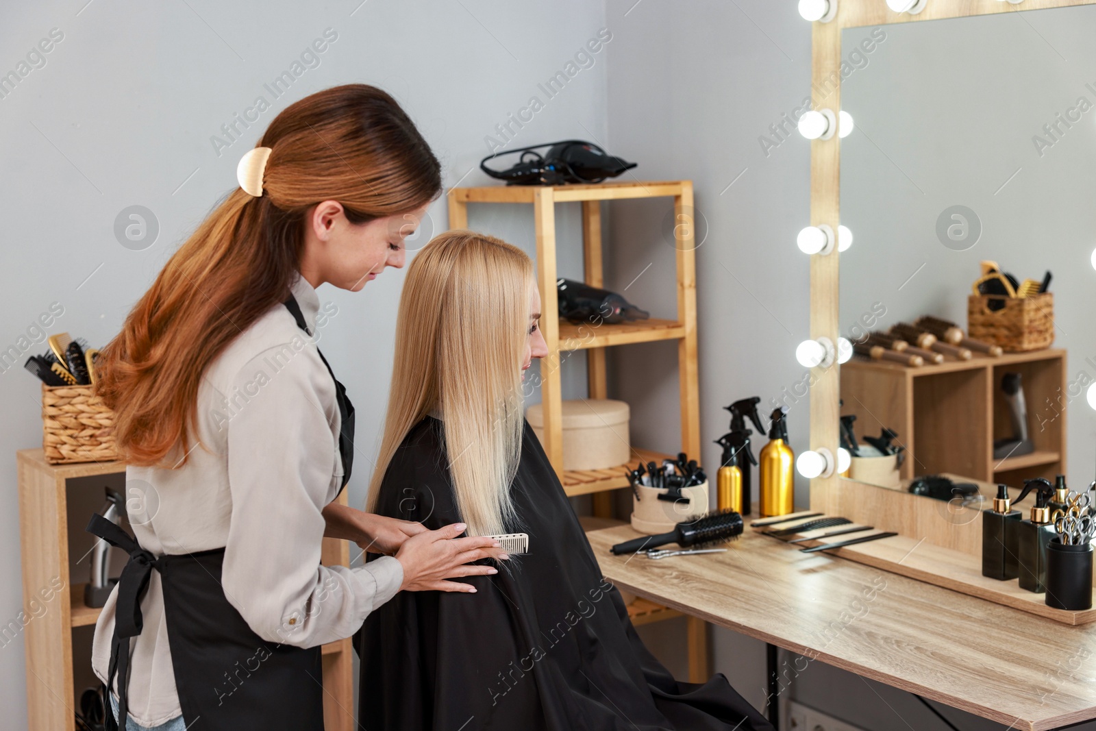 Photo of Professional hairdresser combing woman's hair in salon