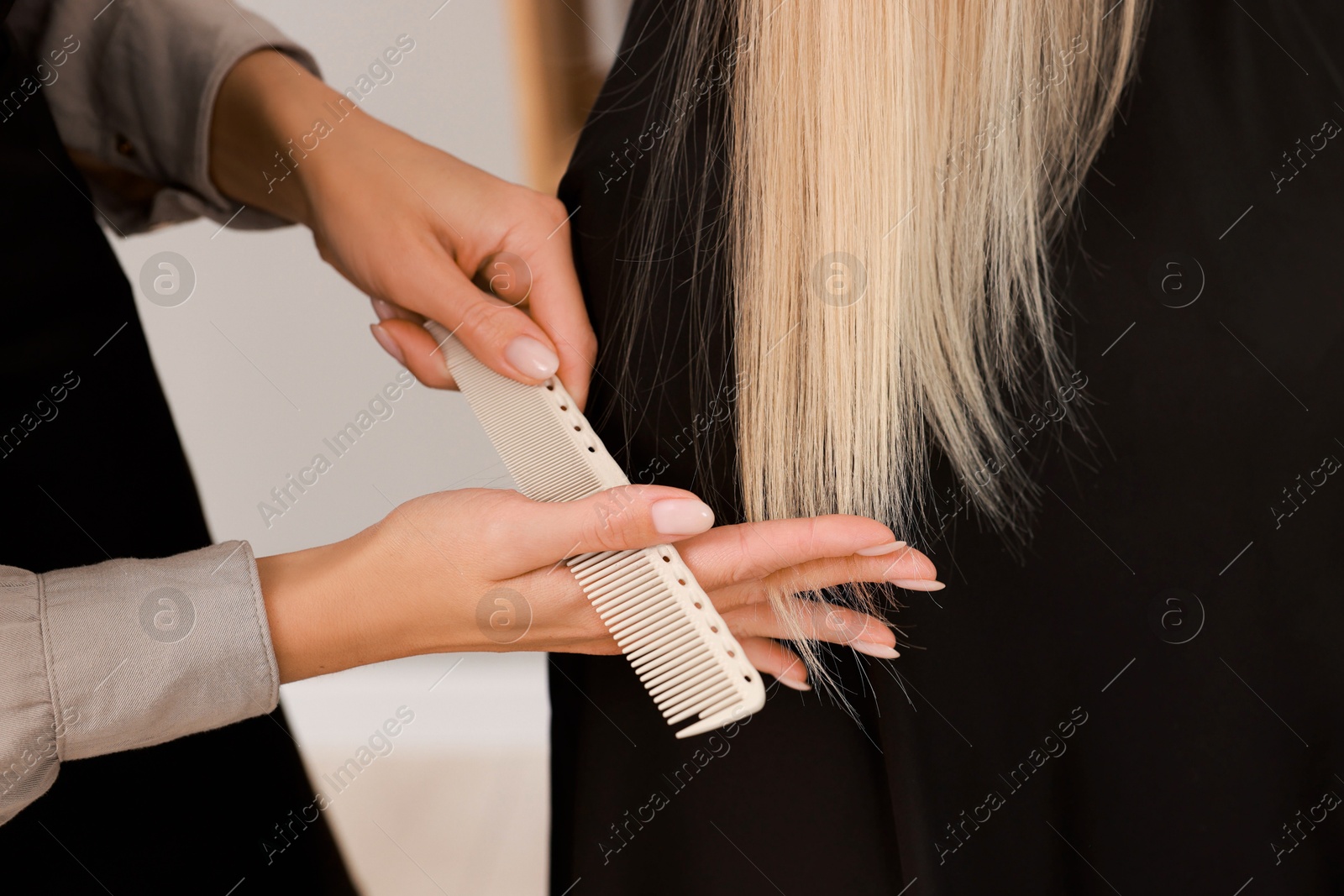 Photo of Hairdresser combing woman's hair in salon, closeup