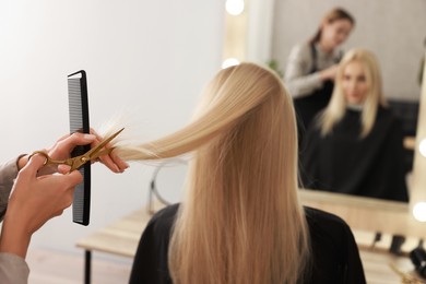 Photo of Hairdresser cutting client's hair with scissors in salon, closeup