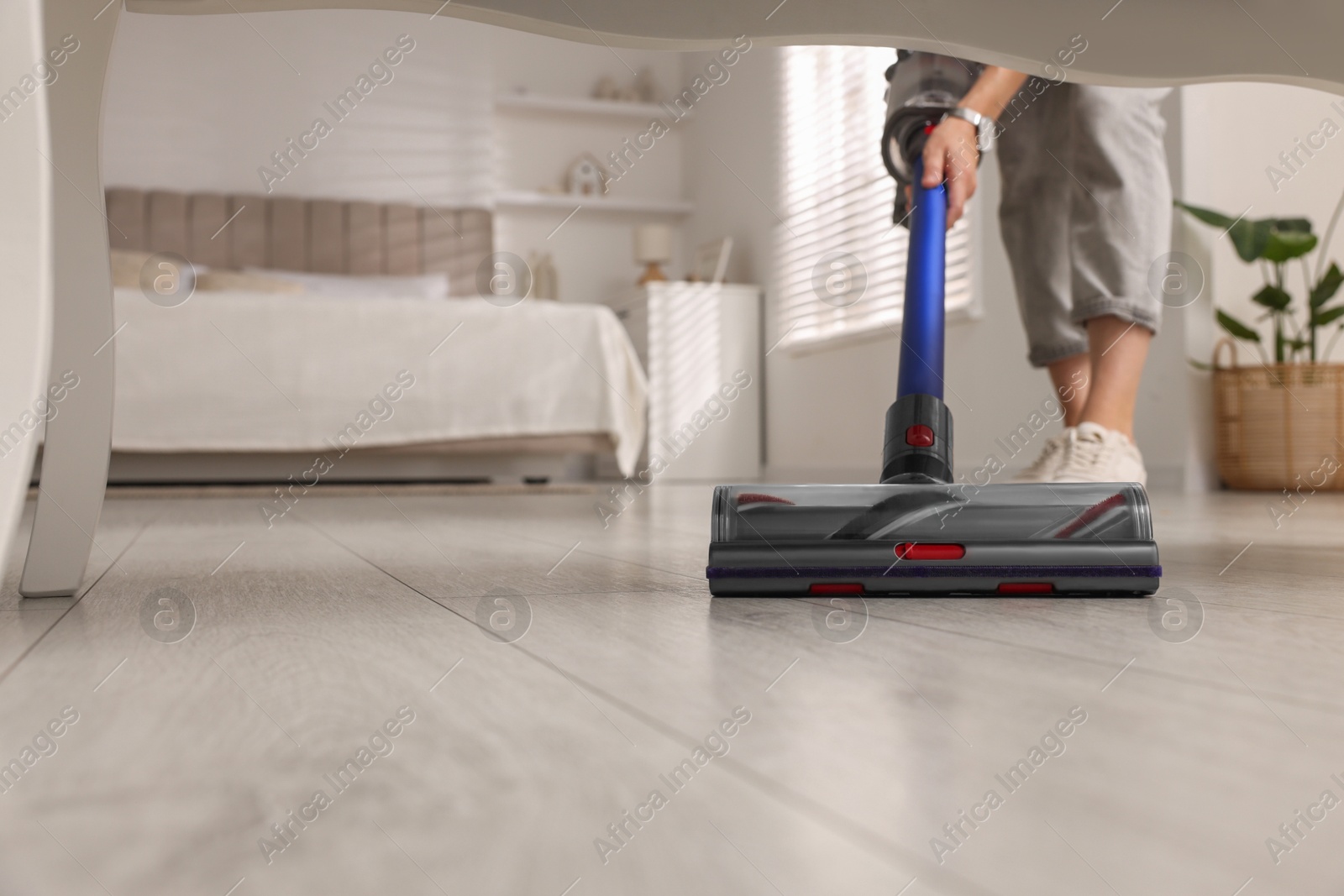 Photo of Woman cleaning floor with cordless vacuum cleaner in bedroom, closeup. Space for text