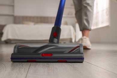 Photo of Woman cleaning floor with cordless vacuum cleaner in bedroom, closeup