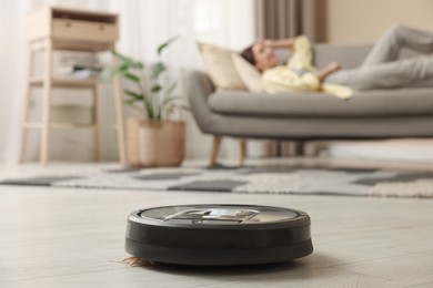 Photo of Young woman resting at home, focus on robotic vacuum cleaner