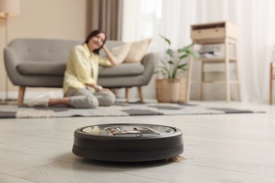 Photo of Young woman resting at home, focus on robotic vacuum cleaner