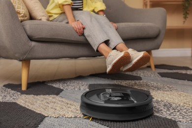 Photo of Young woman resting at home, focus on robotic vacuum cleaner