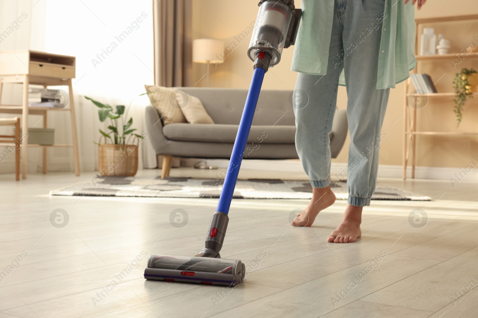 Photo of Woman cleaning floor with cordless vacuum cleaner at home, closeup