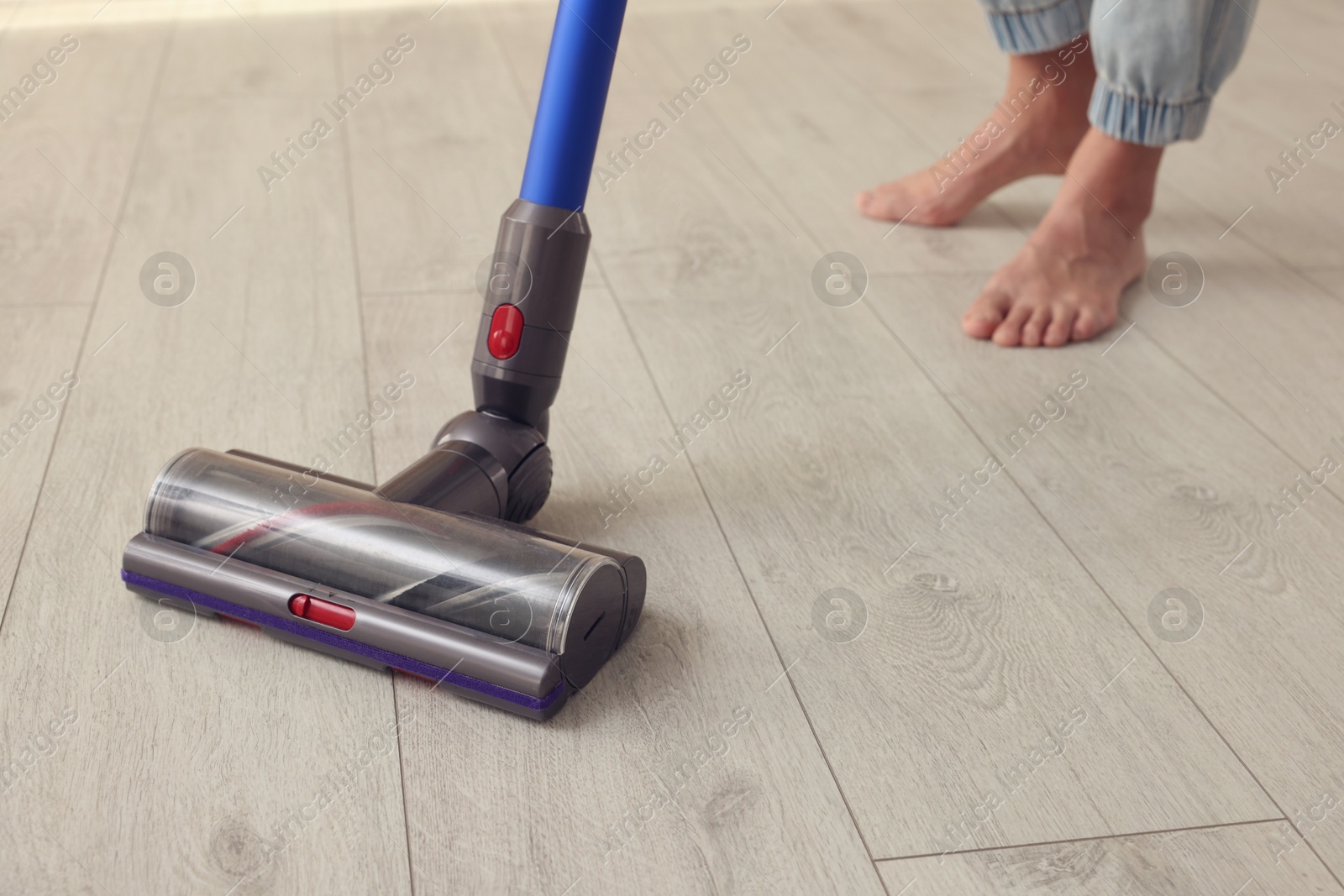 Photo of Woman cleaning floor with cordless vacuum cleaner at home, closeup