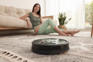 Photo of Young woman resting at home, focus on robotic vacuum cleaner