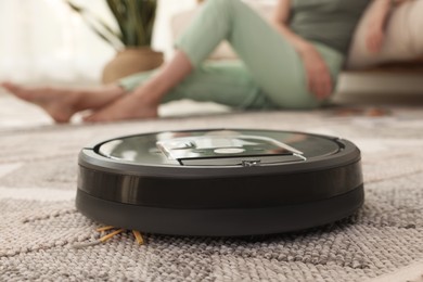 Photo of Young woman resting at home, focus on robotic vacuum cleaner