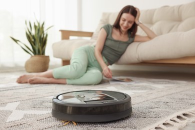 Photo of Young woman resting at home, focus on robotic vacuum cleaner