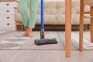 Photo of Woman cleaning rug with cordless vacuum cleaner at home, closeup