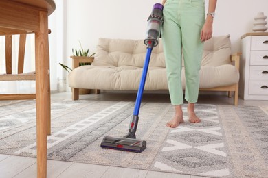 Photo of Woman cleaning rug with cordless vacuum cleaner at home, closeup