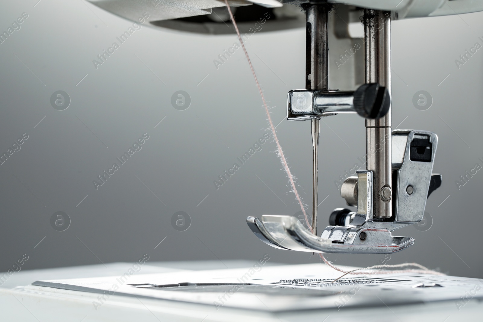 Photo of Sewing machine with white thread on light grey background, macro view. Space for text