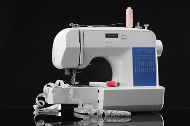 Photo of Sewing machine with measuring tape and spools of threads on black background