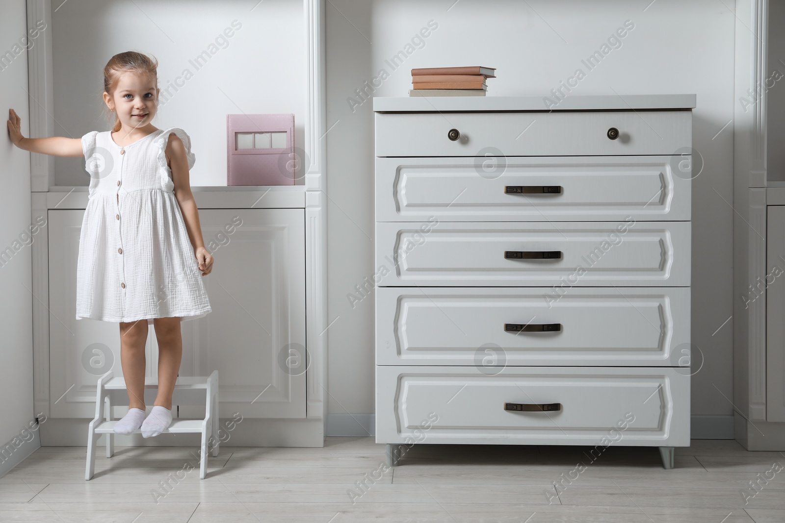 Photo of Little girl standing on step stool indoors, space for text