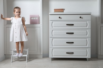 Photo of Little girl standing on step stool indoors, space for text