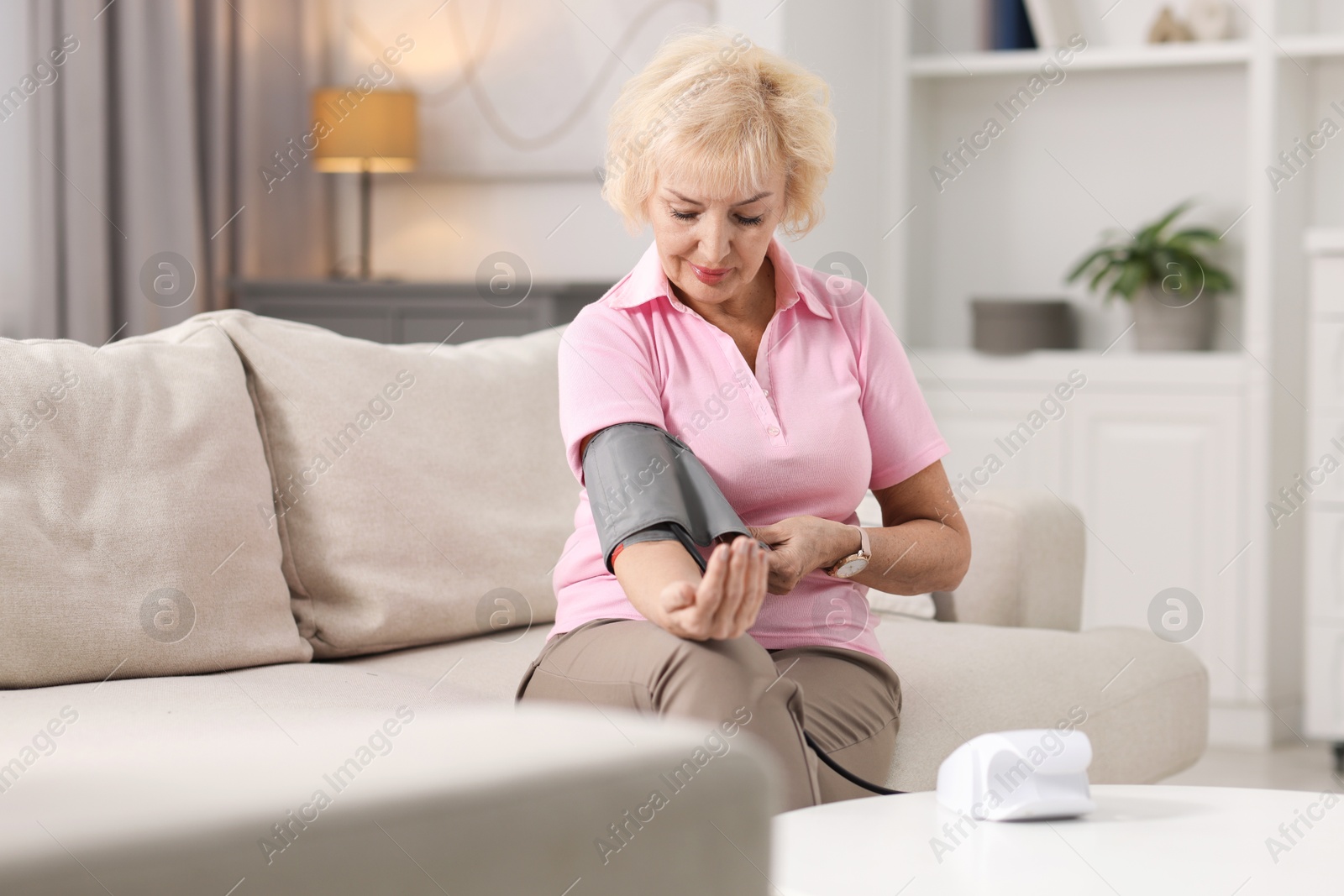 Photo of Senior woman measuring blood pressure on sofa at home