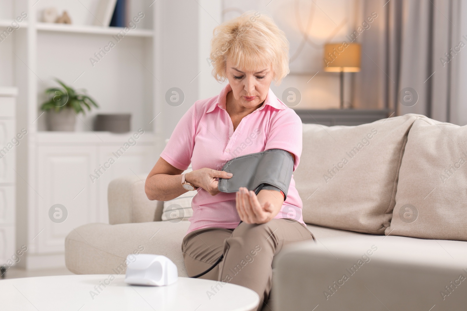 Photo of Senior woman measuring blood pressure on sofa at home