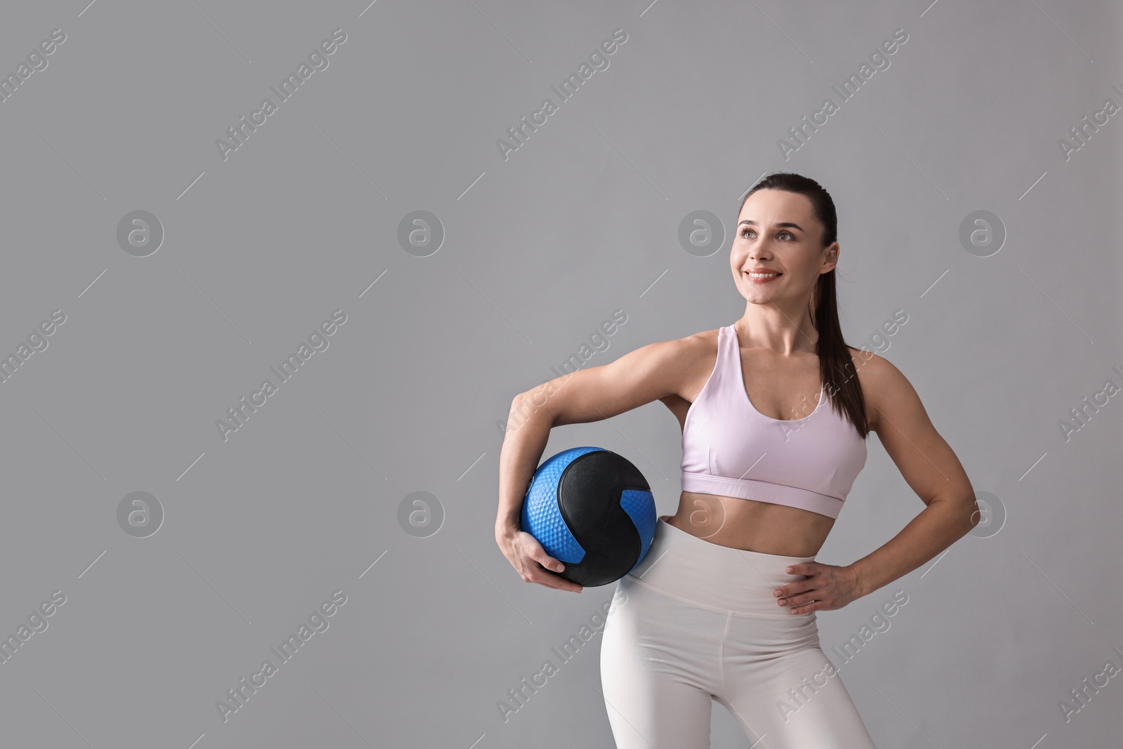 Photo of Woman in gym clothes doing exercise with medicine ball on grey background, space for text