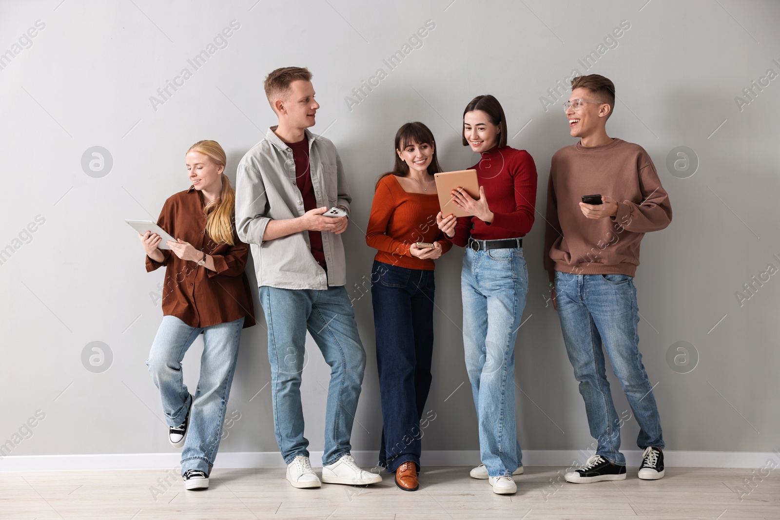 Photo of Group of people using different gadgets near light grey wall indoors. Modern technology