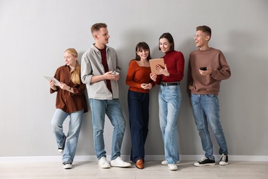 Group of people using different gadgets near light grey wall indoors. Modern technology