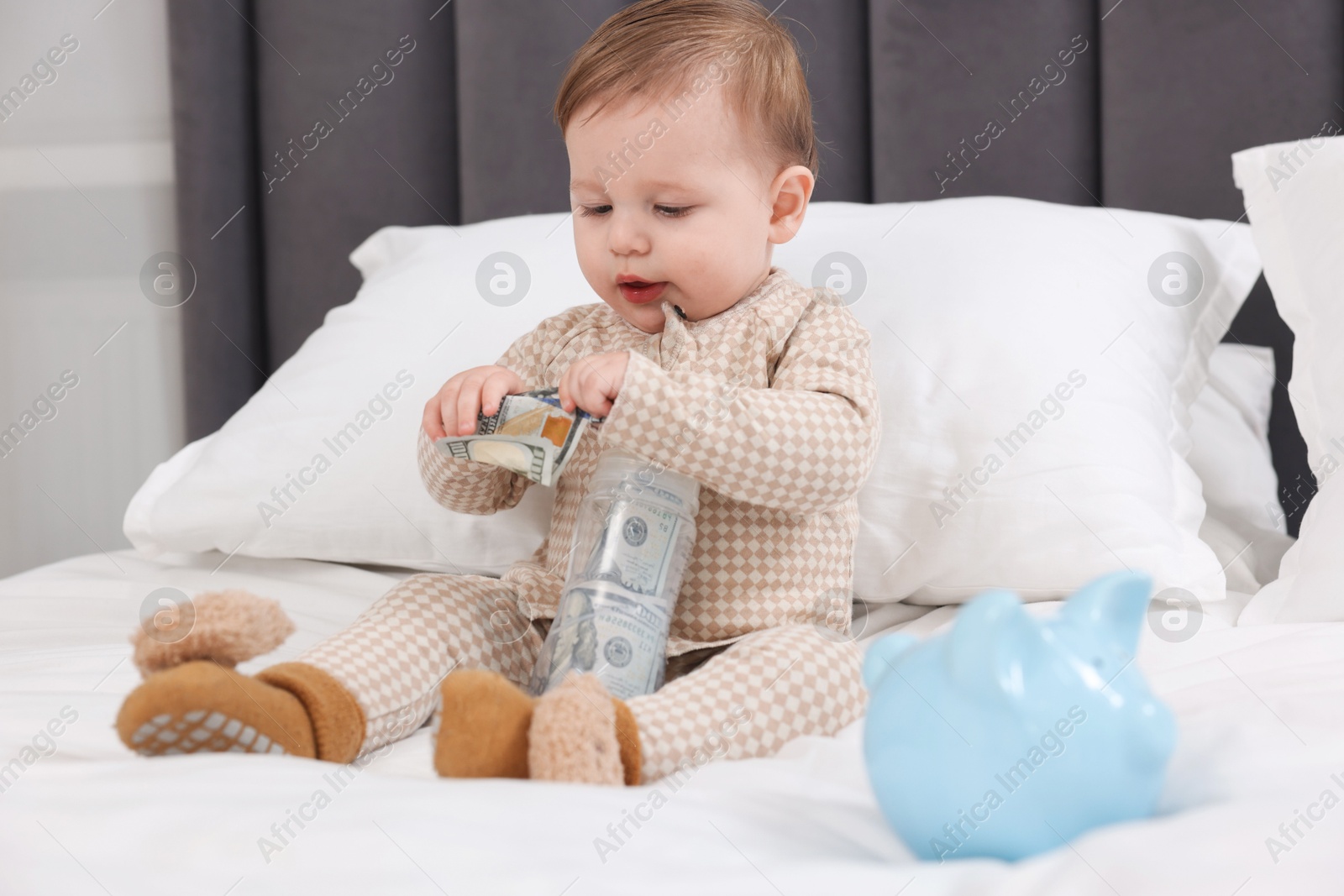 Photo of Cute little baby with money in bottle and piggybank on bed at home