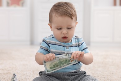 Photo of Little baby with dollar banknote on floor at home