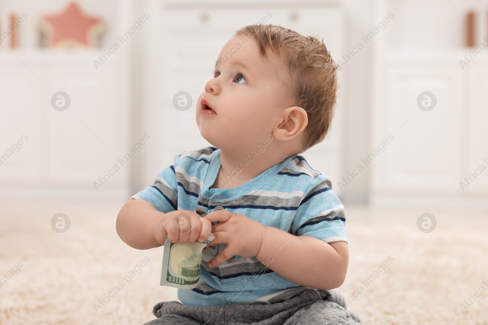 Photo of Little baby with dollar banknote on floor at home