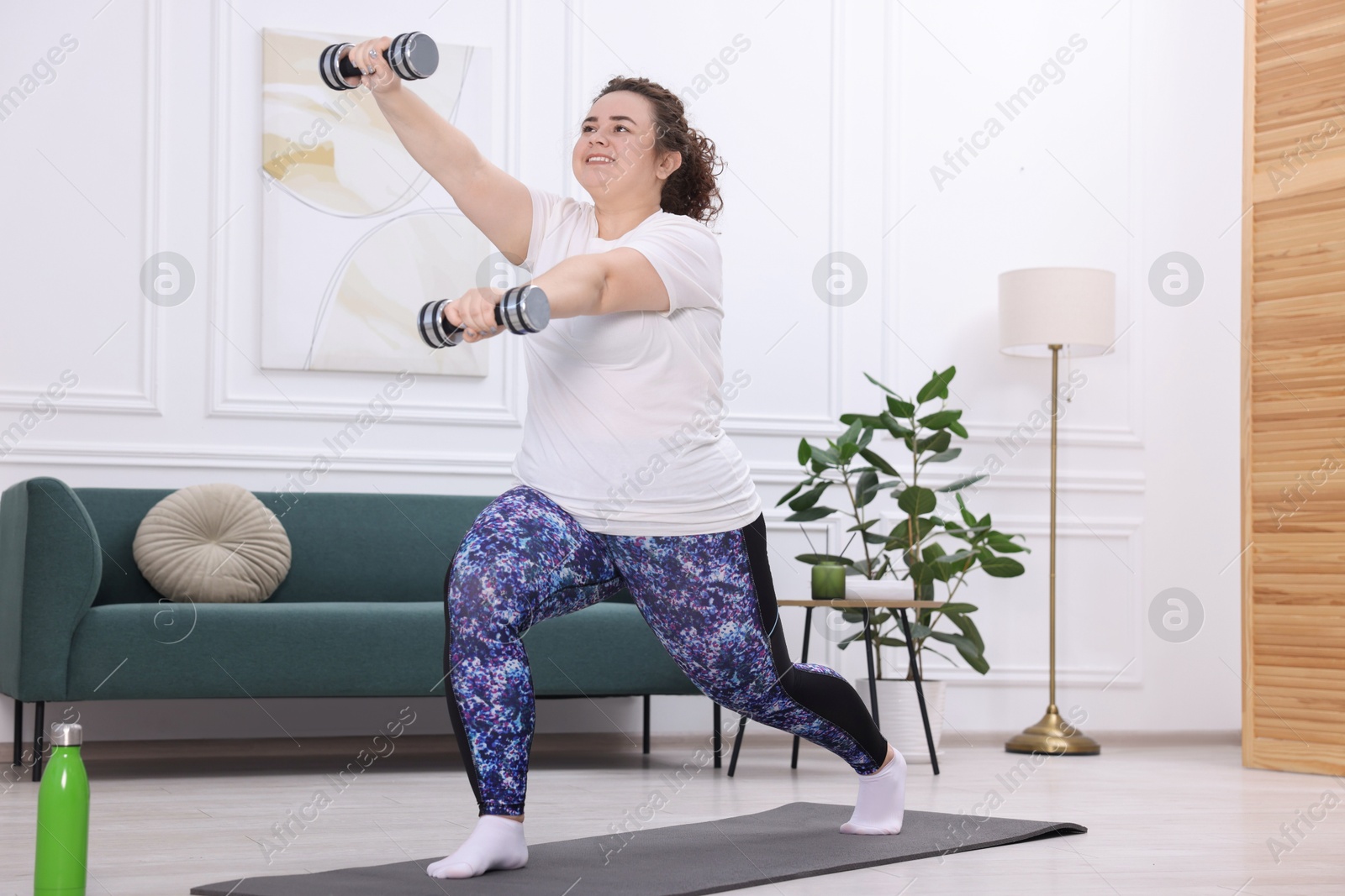 Photo of Plus size woman with dumbbells training at home