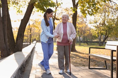 Photo of Elderly woman with walking cane and her caregiver in park