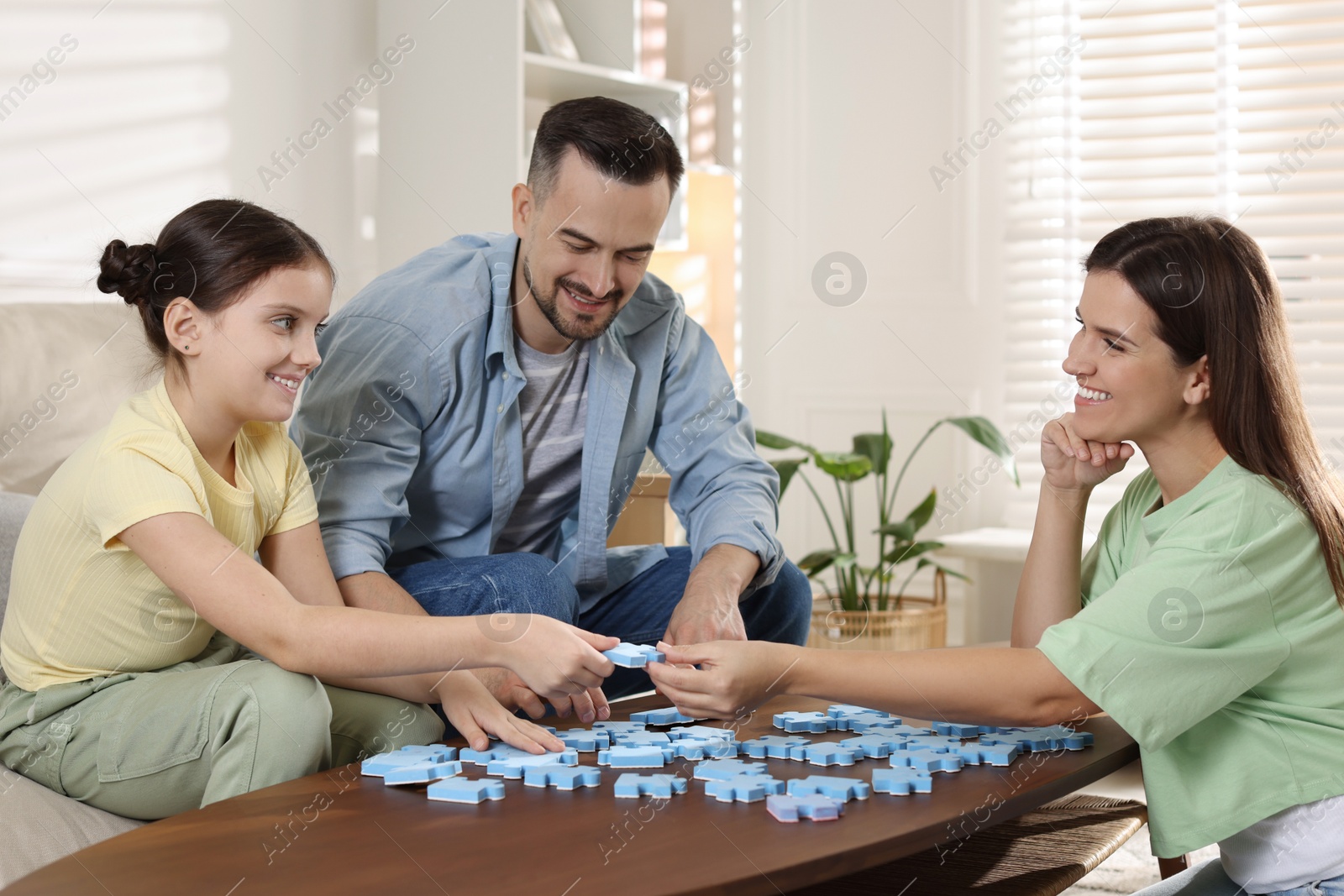 Photo of Happy parents and their daughter solving puzzle together at wooden table indoors