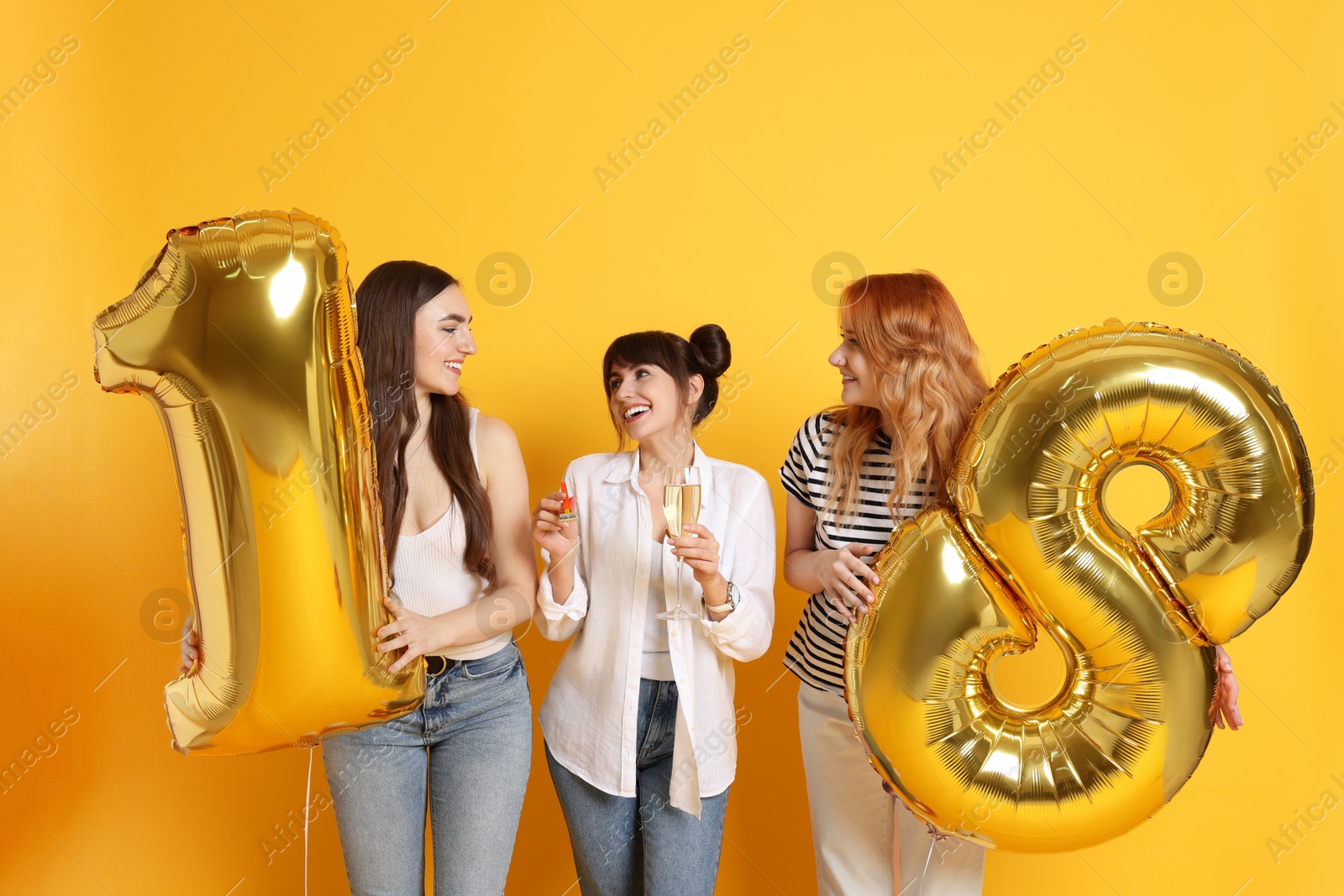 Photo of Coming of age party - 18th birthday. Group of young women celebrating with number shaped balloons on yellow background