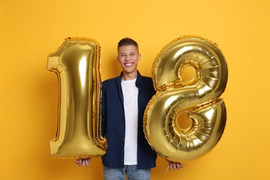 Photo of Coming of age party - 18th birthday. Happy young man with number shaped balloons on yellow background