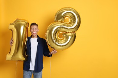 Photo of Coming of age party - 18th birthday. Happy young man with number shaped balloons on yellow background, space for text