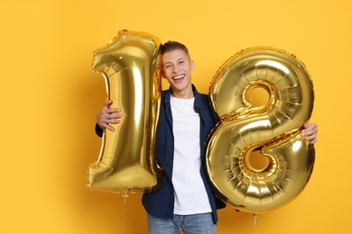 Photo of Coming of age party - 18th birthday. Happy young man with number shaped balloons on yellow background