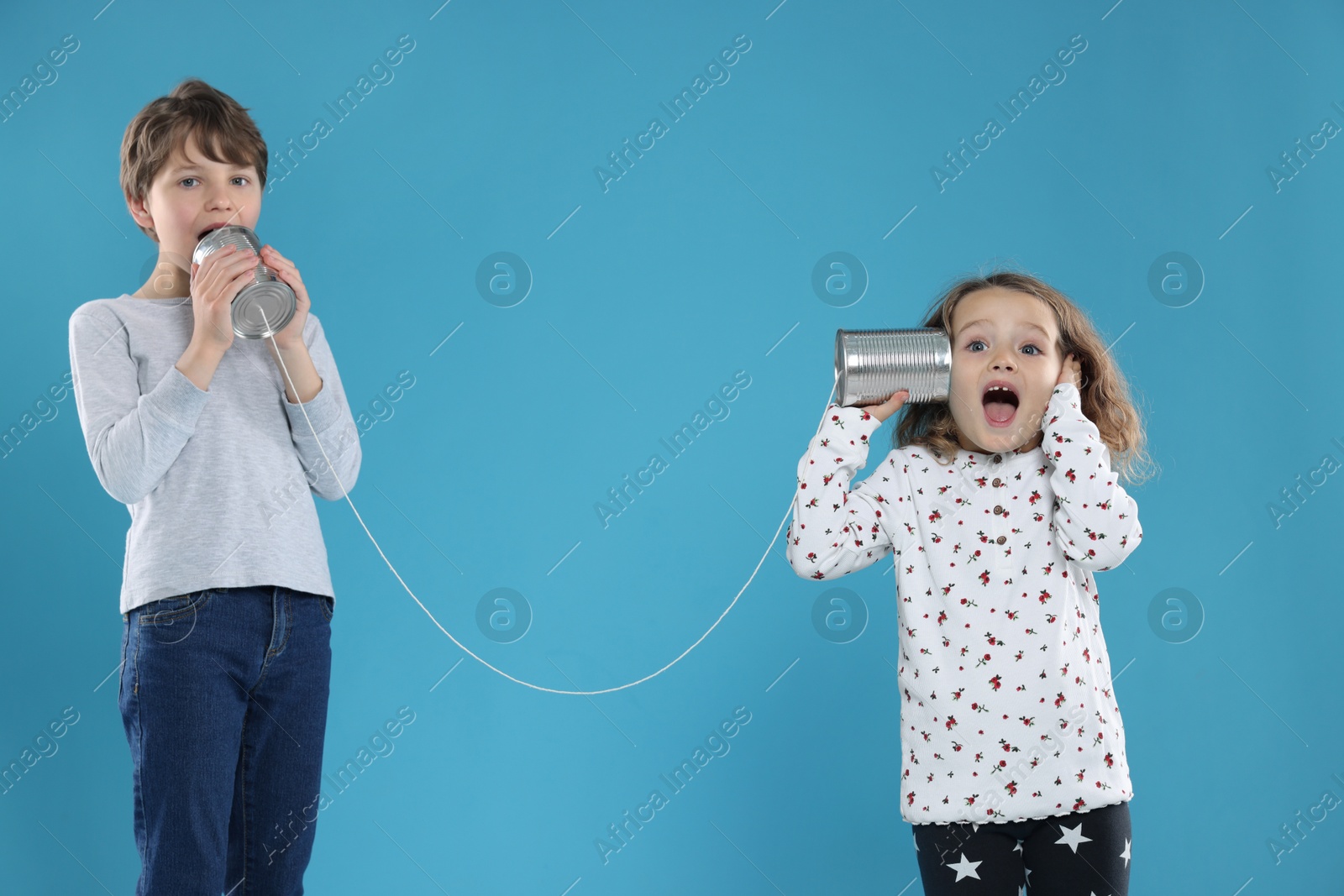 Photo of Boy and girl talking on tin can telephone against blue background