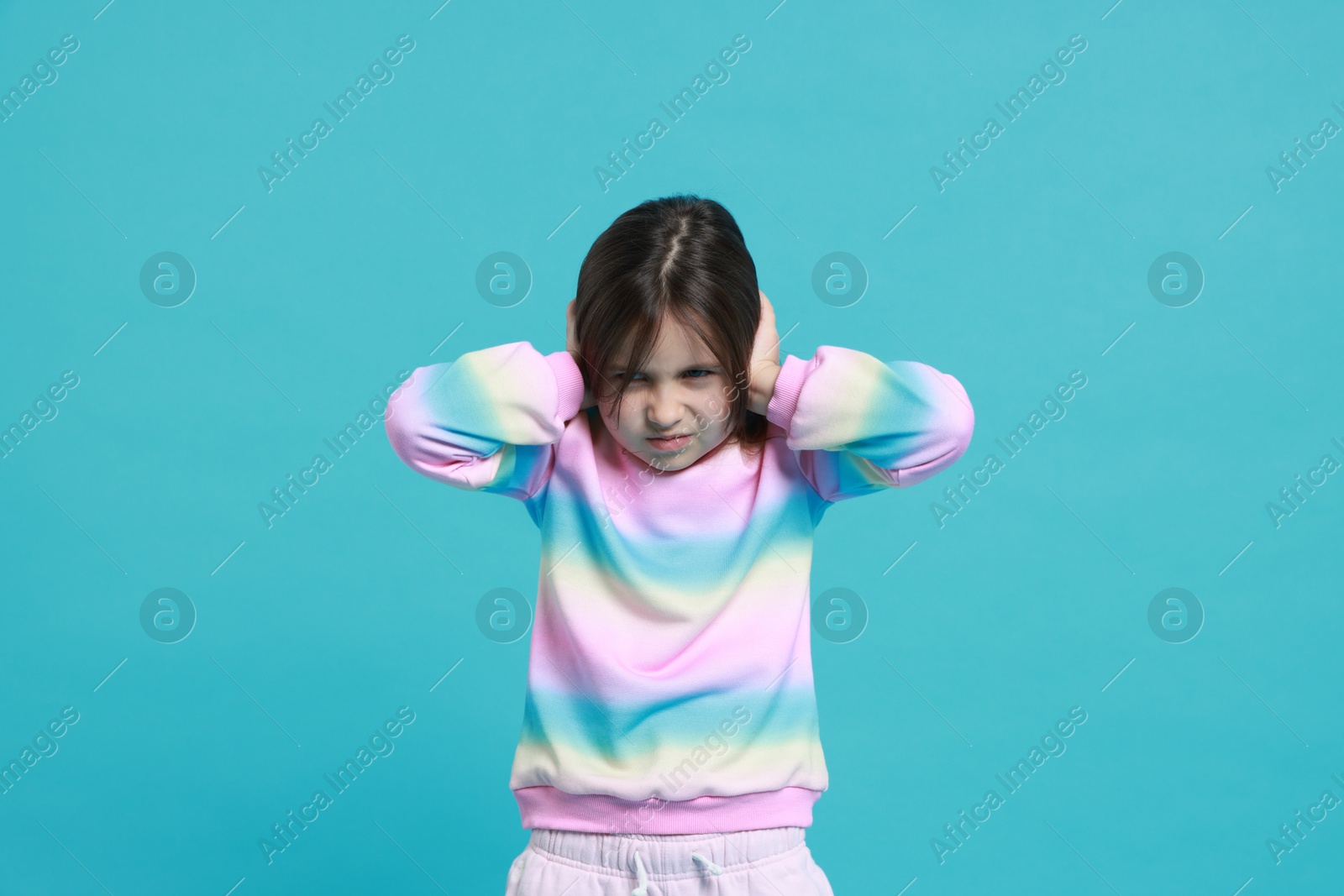 Photo of Annoyed little girl covering her ears from loud sound on light blue background