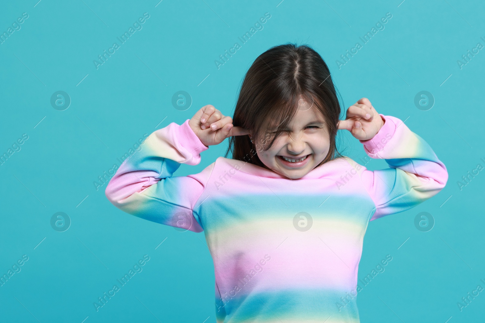 Photo of Annoyed little girl covering her ears from loud sound on light blue background. Space for text