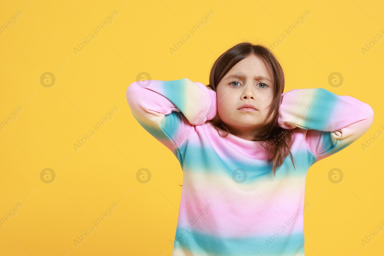 Photo of Exhausted little girl covering her ears from loud sound on yellow background. Space for text