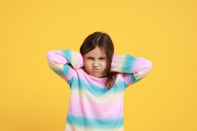 Photo of Annoyed little girl covering her ears from loud sound on yellow background