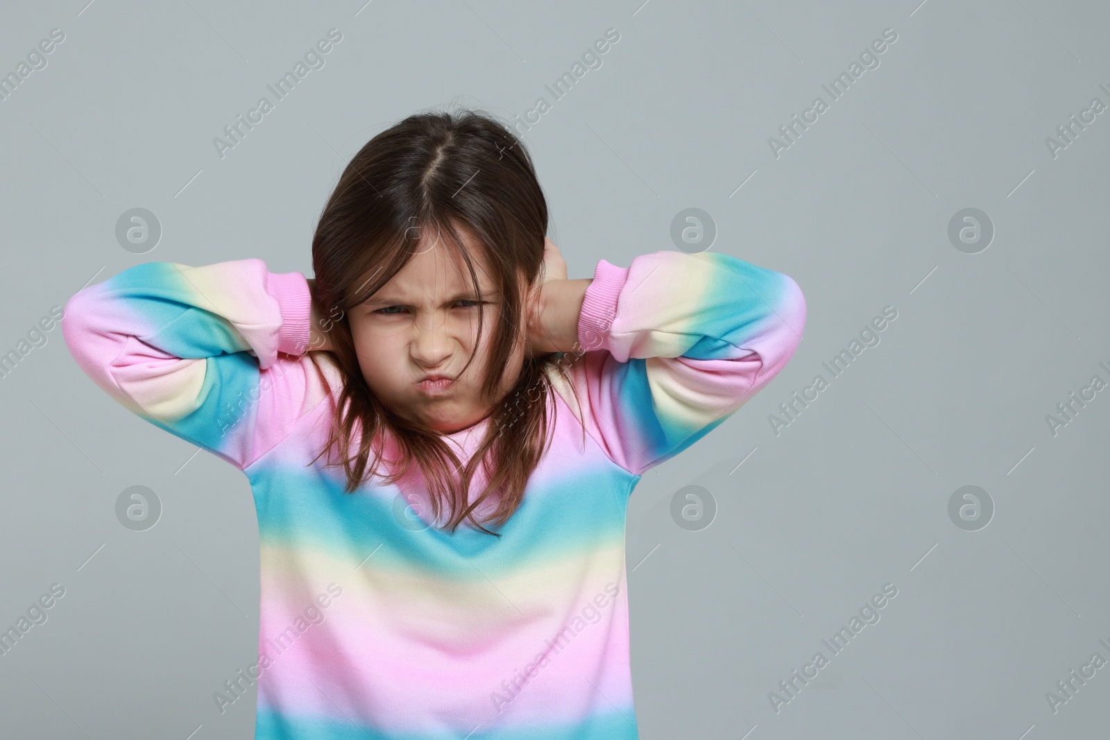 Photo of Annoyed little girl covering her ears from loud sound on grey background. Space for text