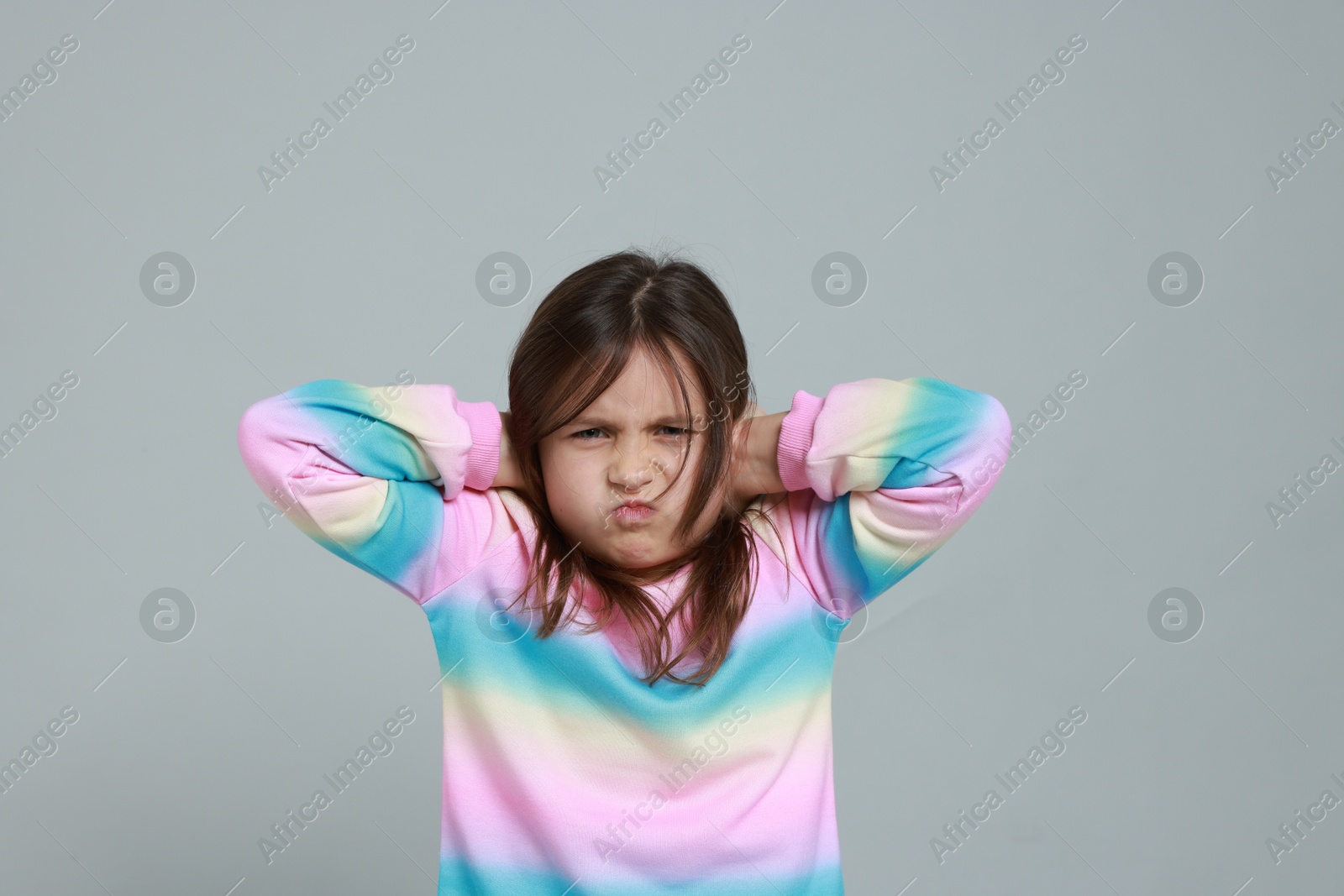 Photo of Annoyed little girl covering her ears from loud sound on grey background