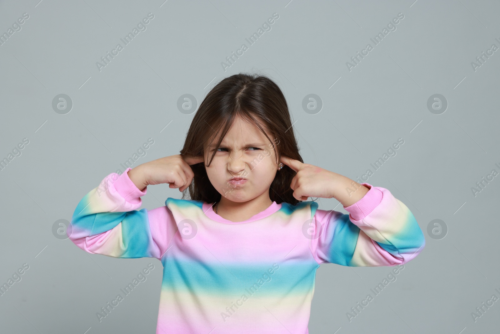 Photo of Annoyed little girl covering her ears from loud sound on grey background