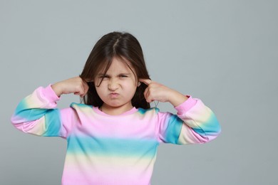 Photo of Annoyed little girl covering her ears from loud sound on grey background. Space for text