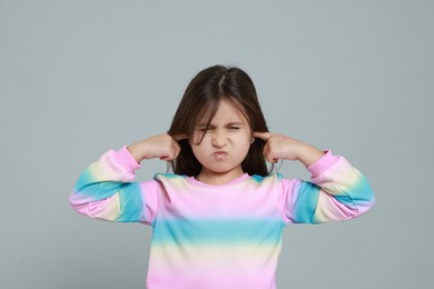 Photo of Annoyed little girl covering her ears from loud sound on grey background