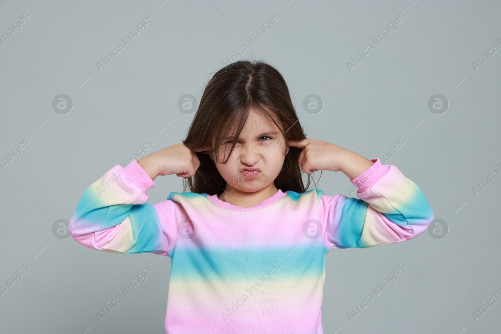 Photo of Annoyed little girl covering her ears from loud sound on grey background