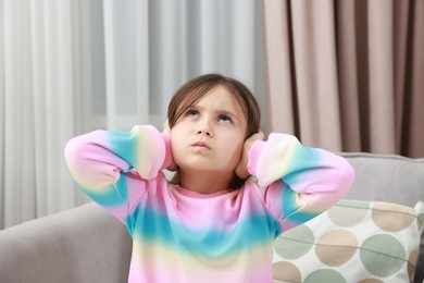 Photo of Annoyed little girl covering her ears with pillows from loud sound on armchair at home